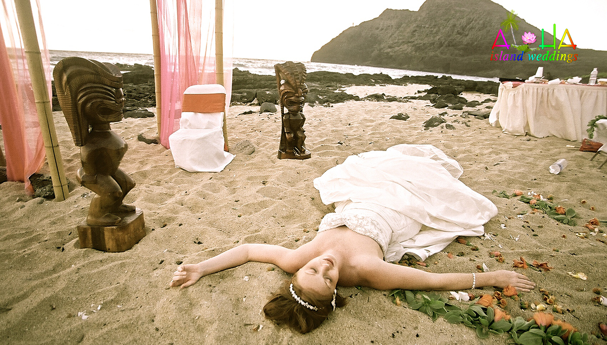 sleeping beauty laying on the sand after her beach wedding ceremony with Hawaiian Tiki